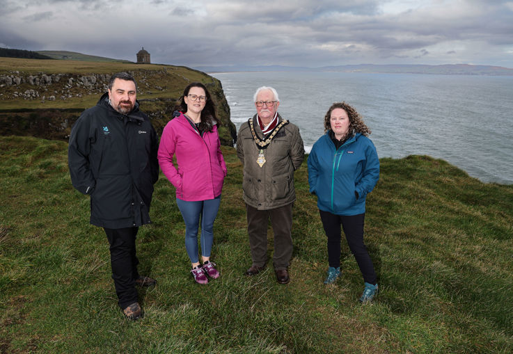 A group of 4 individuals standing together on a cliff, with the sea visible in the background, smiling at the camera.